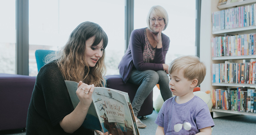 A woman reading a book to a young boy