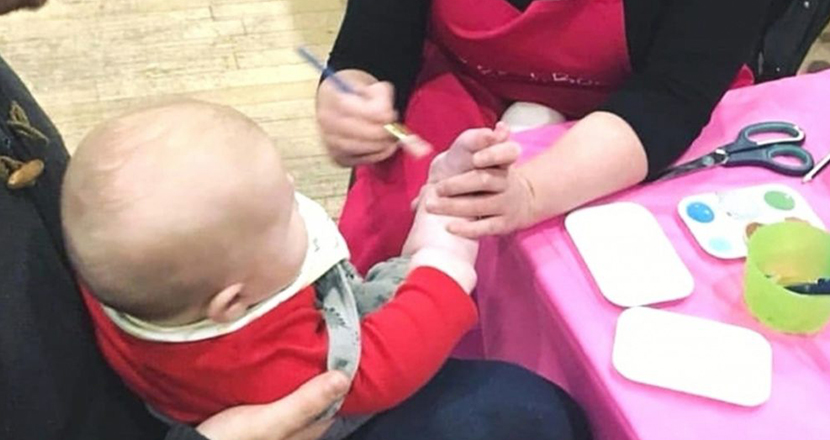 A photograph of a baby having his feet painted